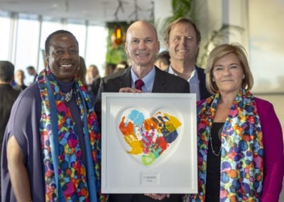 four people smiling and holding a painting of children's handprints